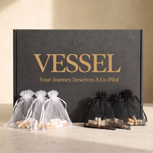 A black presentation box with gold lettering reading 'VESSEL' and 'Your Journey Deserves A Co-Pilot' sits on a light surface. Three sheer white drawstring pouches and three sheer black drawstring pouches containing capsules are arranged in front of the box.